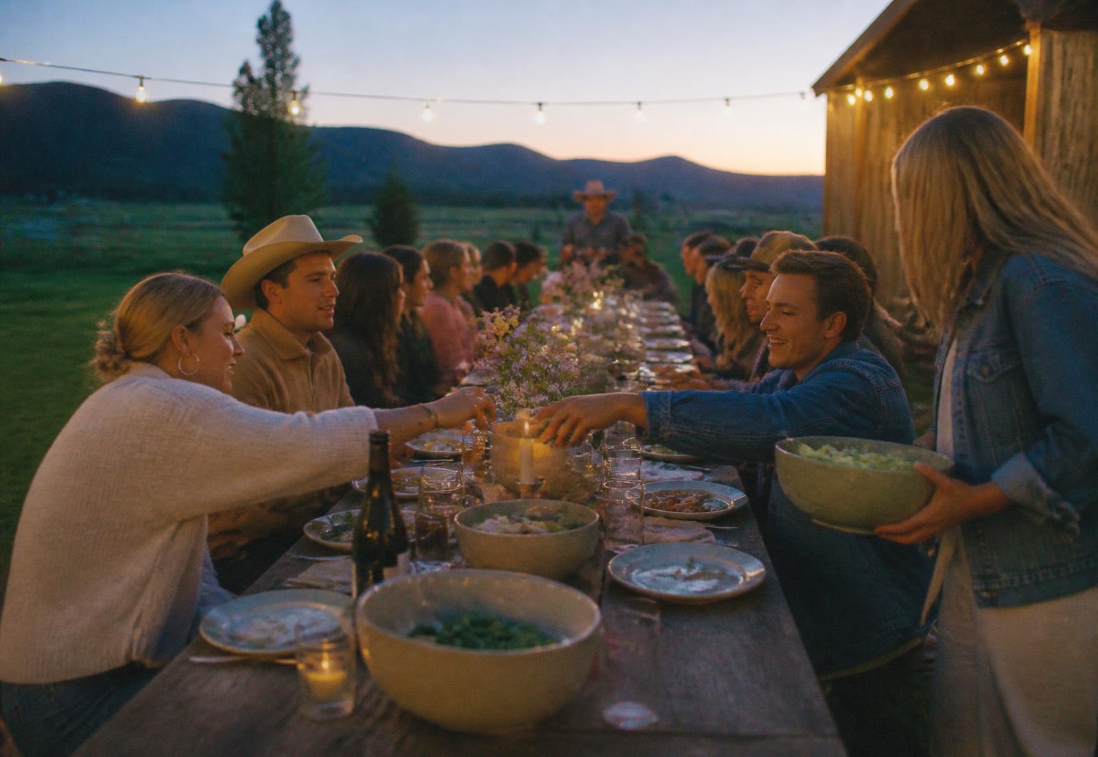 A long communal dinner table outdoors at dusk